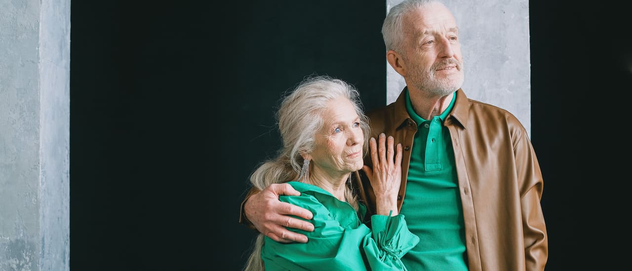 An older man and woman standing close together, both looking off into the distance.